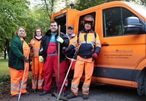 Fünf Personen stehen mit Arbeitsutensilien vor einem Fahrzeug der Stadtverwaltung. 