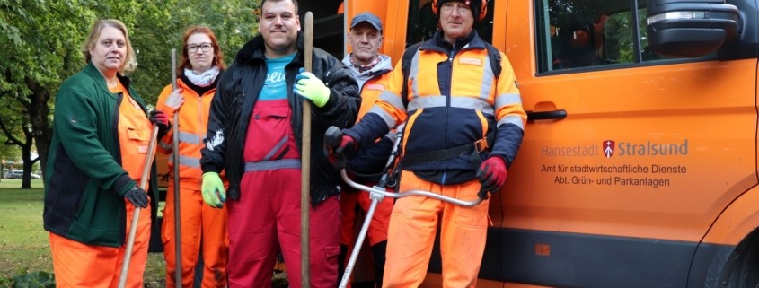 Fünf Personen stehen mit Arbeitsutensilien vor einem Fahrzeug der Stadtverwaltung.