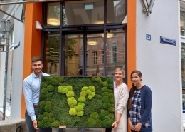 Zwei Personen halten ein Moosbild in der Hand. Darauf zu sehen ist das Logo der Bank.
