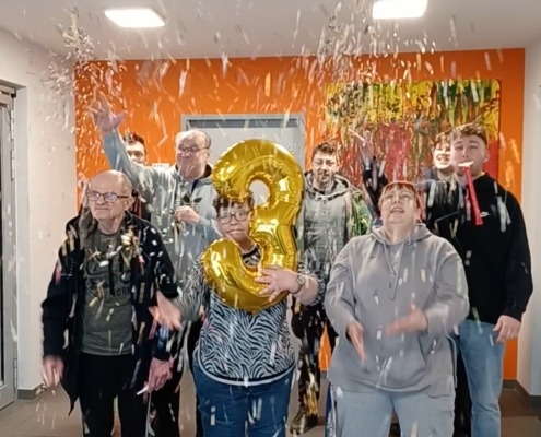 Mehrere Wohnhausbewohner und -betreuer werfen Konfetti in die Luft.