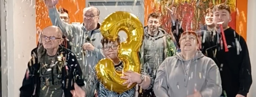 Mehrere Wohnhausbewohner und -betreuer werfen Konfetti in die Luft.