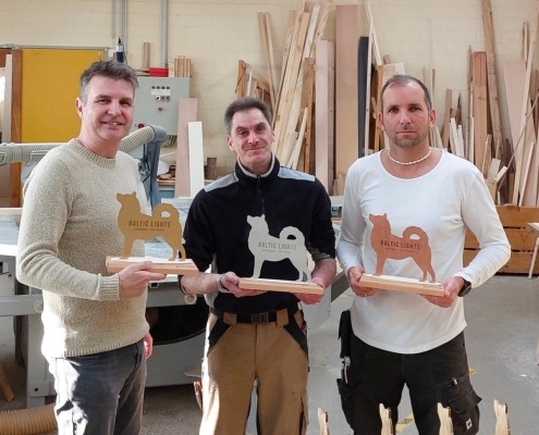 Drei Mitarbeiter der Tischlerei halten Pokale in Hundeform für die Veranstaltung Baltic Lights Usedom in den Händen.