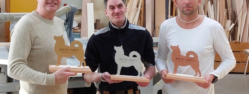 Drei Mitarbeiter der Tischlerei halten Pokale in Hundeform für die Veranstaltung Baltic Lights Usedom in den Händen.