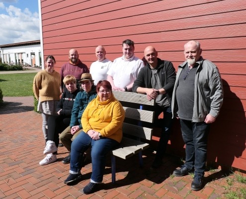 Drei Personen sitzen auf einer Bank und sechs Personen stehen dahinter.