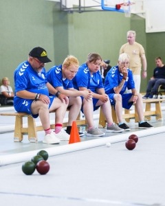 Vier Personen der Stralsunder Werkstätten blicken gespannt auf die rollenden Bocciakugeln.