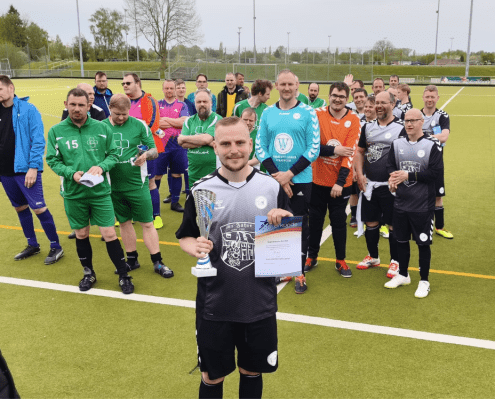 Ein Spieler der Fußballmannschaft der Stralsunder Werkstätten steht vor seinem Team und hält einen Pokal und die Urkunde in den Händen.