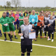 Ein Spieler der Fußballmannschaft der Stralsunder Werkstätten steht vor seinem Team und hält einen Pokal und die Urkunde in den Händen.