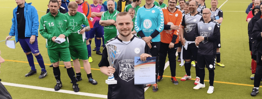 Ein Spieler der Fußballmannschaft der Stralsunder Werkstätten steht vor seinem Team und hält einen Pokal und die Urkunde in den Händen.