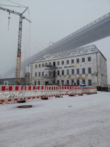 Die neue Betriebsstätte der Stralsunder Werkstätten mitten im Baugeschehen befindet sich im dichten Nebel. Im Vordergrund sind Bauzäune, ein Kran sowie ein Baugerüst zu sehen.