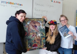 Drei Personen zeigen ein fertiges Puzzle mit Dinosauriermotiv und ein Fachbuch.