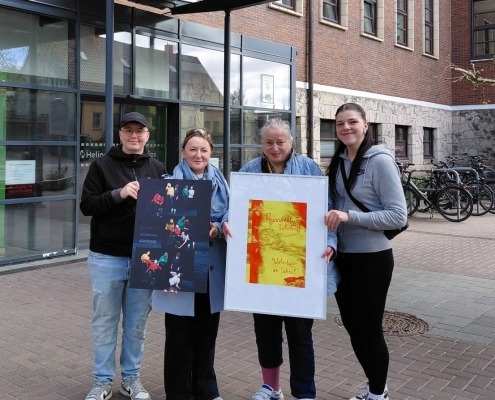 Vier Personen stehen vor dem Helios Hanseklinikum in Stralsund und halten zwei Bilder der Wanderfotoausstellung der Stralsunder Werkstätten in den Händen.