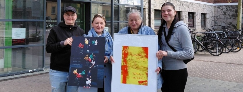 Vier Personen stehen vor dem Helios Hanseklinikum in Stralsund und halten zwei Bilder der Wanderfotoausstellung der Stralsunder Werkstätten in den Händen.