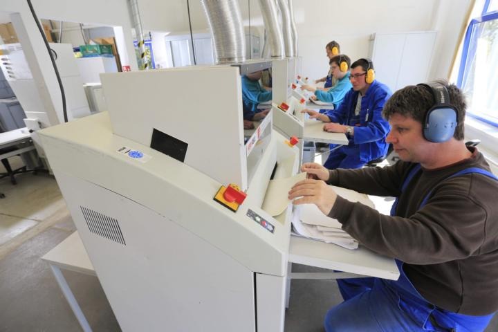 Aktenvernichtung Mehrere Personen mit Gehörschutz vernichten Akten an einer Schreddermaschine.