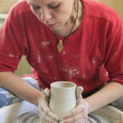 Eine Person arbeitet an einer Drehscheibe und formt mit den Händen Ton zu einer Vase.