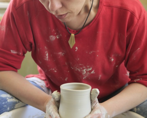 Eine Person arbeitet an einer Drehscheibe und formt mit den Händen Ton zu einer Vase.