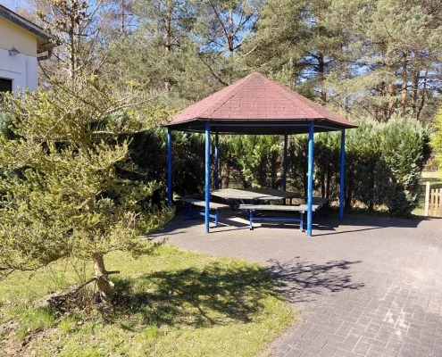 Außengelände_Tagesgruppe_Senioren Im Außenbereich der Tagesgruppe für Senioren steht ein Holzpavillon mit einem Tisch und Sitzbänken.
