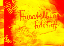 Ein Plakat in rot, orange und gelb mit der Aufschrift "Ausstellung Fototreff". Im Hintergrund sind Büroklammern zu sehen.