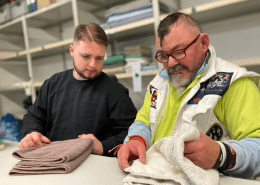 Eine Person zeigt einer zweiten Person, wie Handtücher korrekt gefaltet werden.