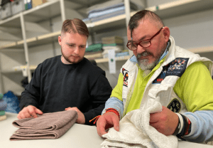 Eine Person zeigt einer zweiten Person, wie Handtücher korrekt gefaltet werden.