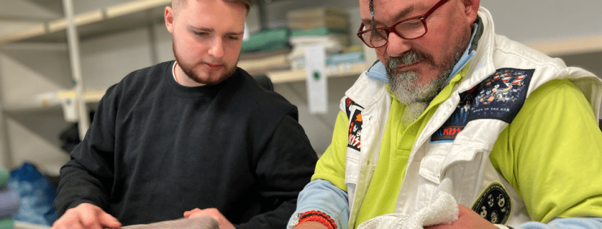 Eine Person zeigt einer zweiten Person, wie Handtücher korrekt gefaltet werden.