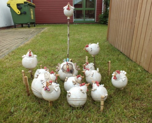 viele weiße dicke Keramikhühner auf einer Rasenfläche; sie sind eingezäunt