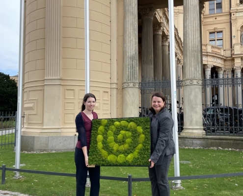 Zwei Personen stehen vor dem Schweriner Schloss und halten ein Moosbild in den Händen.