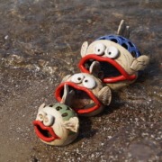 drei Keramikfische mit großem offenen Mund in unterschiedlichen Größen am Strand