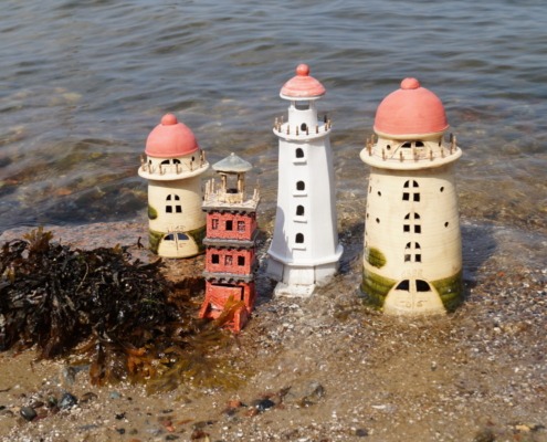 vier Keramikleuchttürme in unterschiedlichen Größen am Strand