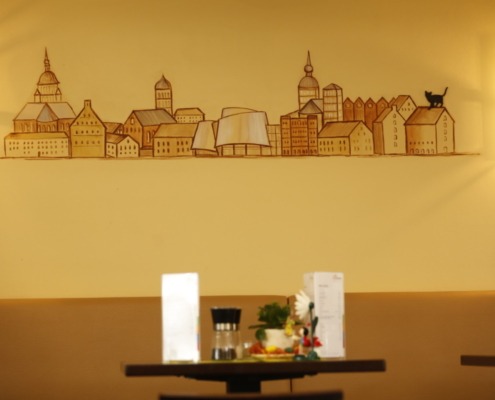 Blick auf eine Wandzeichnung. Zu sehen sind Häuser Stralsunds mit einer Katze auf einem Hausdach.