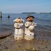 ein Mann und eine Frau aus Keramik am Strand, beide halten je einen Fisch in der Hand
