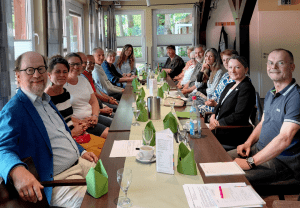 16 Personen sitzen an einer Tafel und tauschen sich über Inklusionsthemen aus.