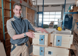 Eine Person steht an einer voll beladenen Palette mit fertigen Nistkästen für Wildvögel.