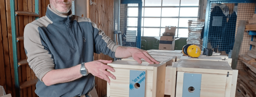 Eine Person steht an einer voll beladenen Palette mit fertigen Nistkästen für Wildvögel.