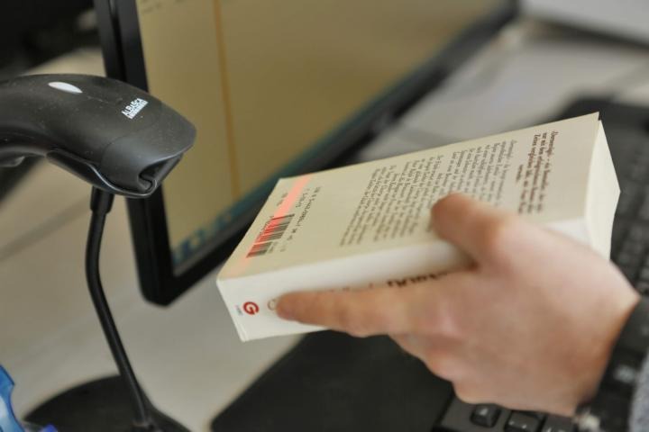 Online Buchhandel Eine Hand hält ein Buch unter den Scanner.