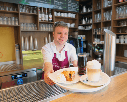 Service_Delikater Eine Person serviert im Bistro ein Kaffeegedeck.
