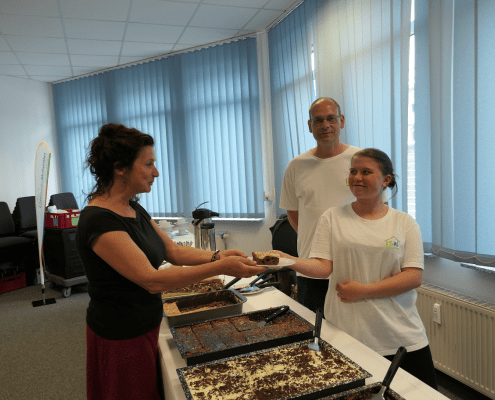 Zwei Personen des Berufsbildungsbereichs servieren einem Gast ein Stück Kuchen.
