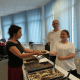 Zwei Personen des Berufsbildungsbereichs servieren einem Gast ein Stück Kuchen.