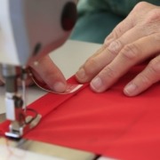 Hände messen den Saum einer roten Bojenflagge mit einem Maßband ab