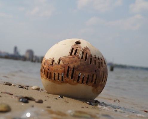 Keramikkugel mit Stralsundmotiv steht im Strandsand