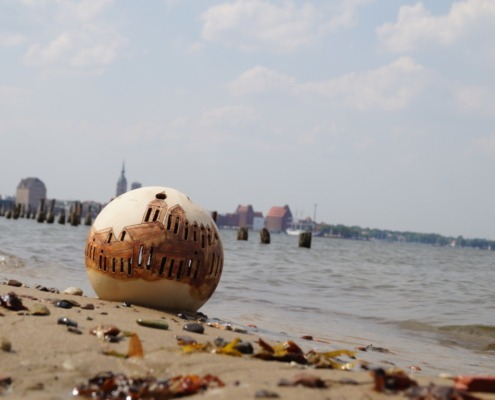 Keramikkugel mit Stralsundmotiv steht im Strandsand
