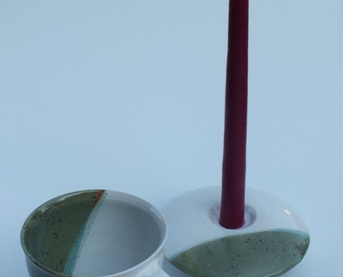 eine Tasse mit Unterteller und passendem Kerzenhalter in teils weiß, teils olivgrün