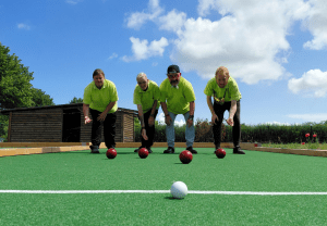 Vier Personen sind auf dem Bocciafeld der Stralsunder Werkstätten und werfen ihre Bocciakugeln in Richtung der Zielkugel.