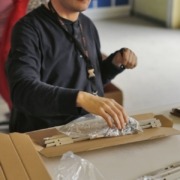 Eine Person verpackt Montageschienen und Zubehörtüten in einen Karton.