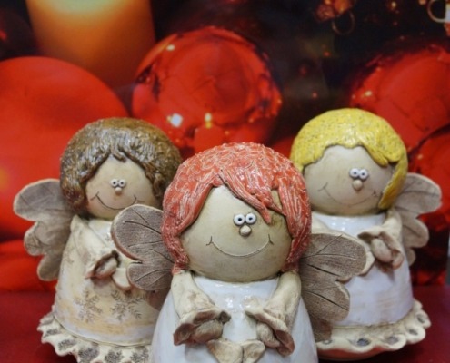 drei Weihnachtsengel aus Keramik, im Hintergrund rote Weihnachtskugeln und eine Kerze