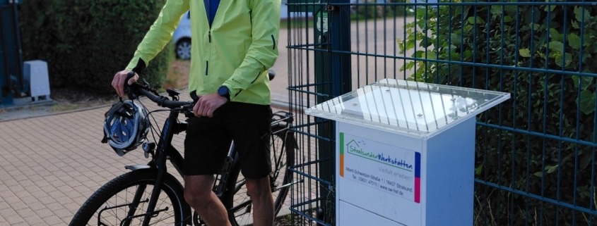 Ein Mann steht mit seinem Fahrrad neben einem Schild, auf dem die Zahl 1 abgebildet ist.