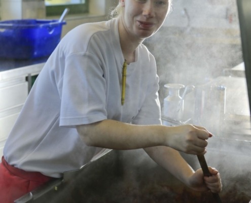 Eine Person rührt in einer sehr großen Pfanne das Essen um.